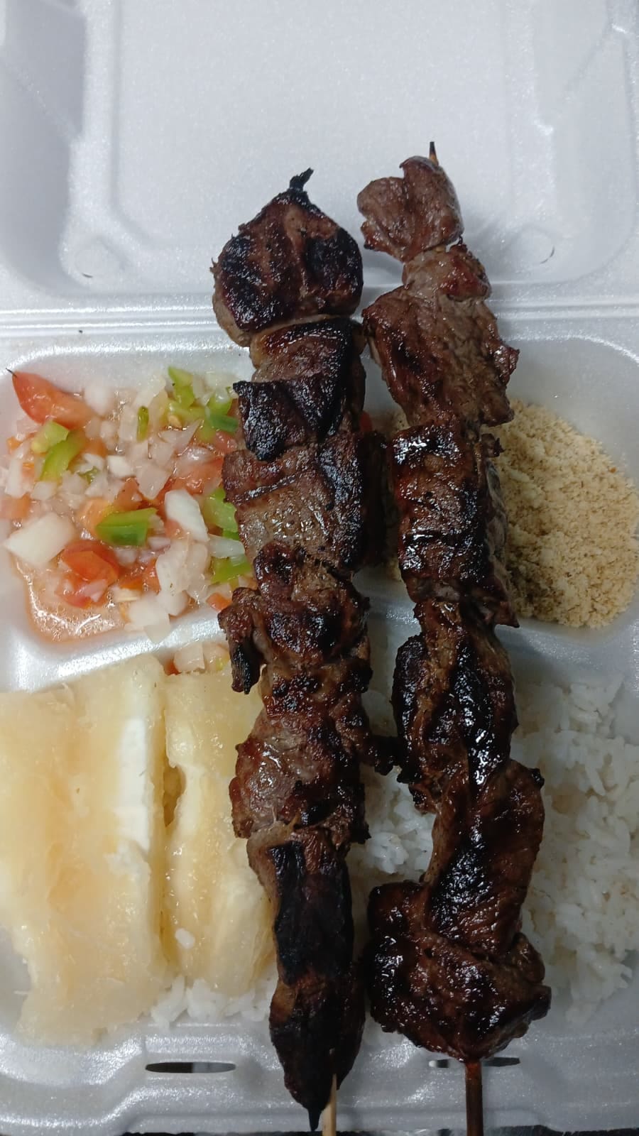 Prato com espetinhos, mandioca, arroz e farofa